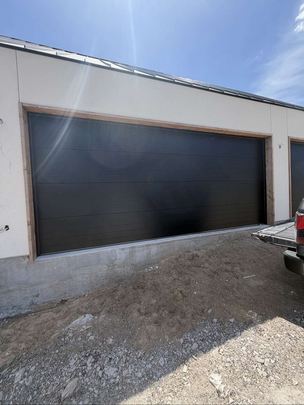 A black flush double garage door newly installed on a white stucco house under construction, in Horseshoe Bay