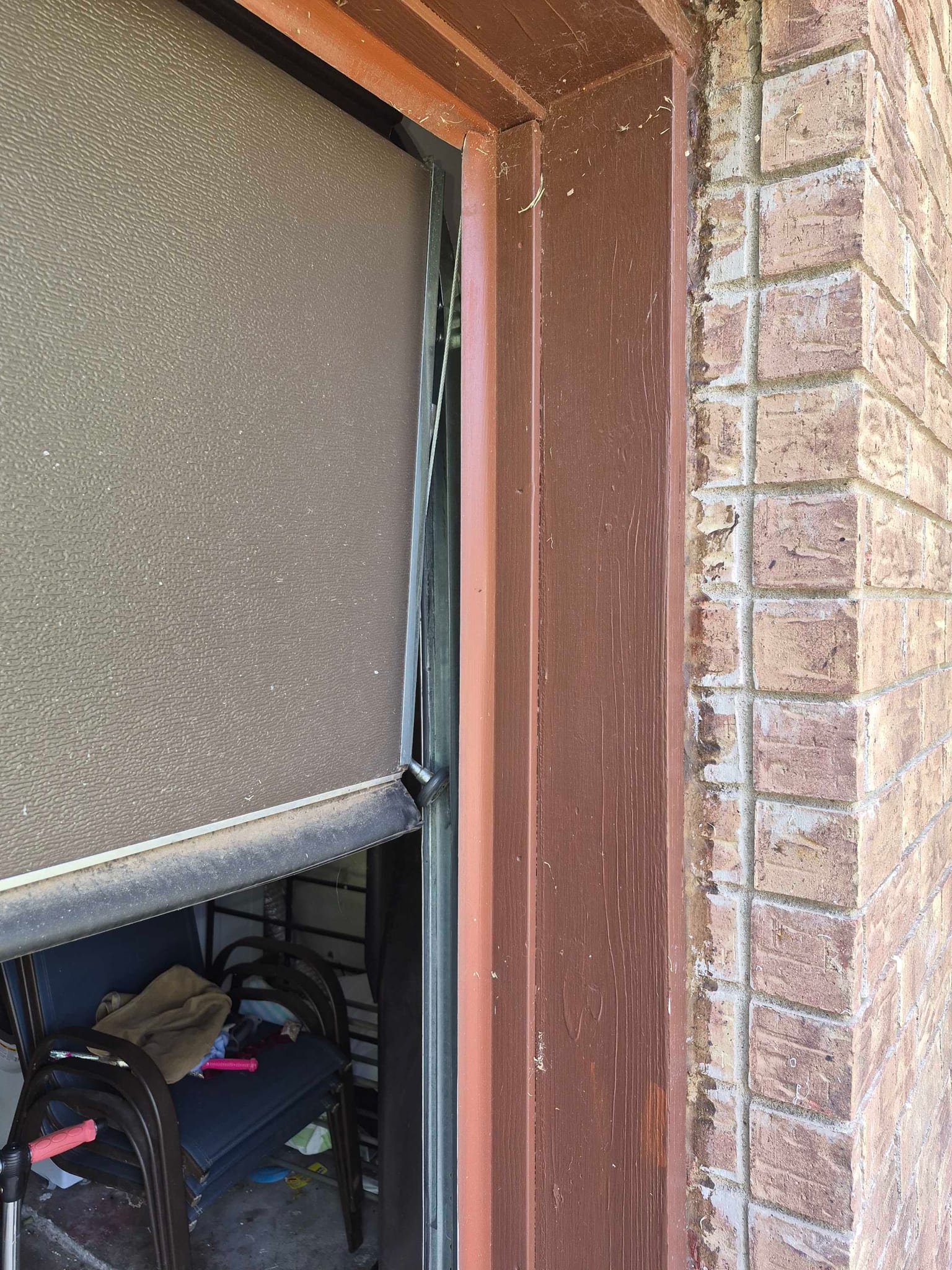 A garage door hanging crooked off its track inside a brown door frame, in Marble Falls