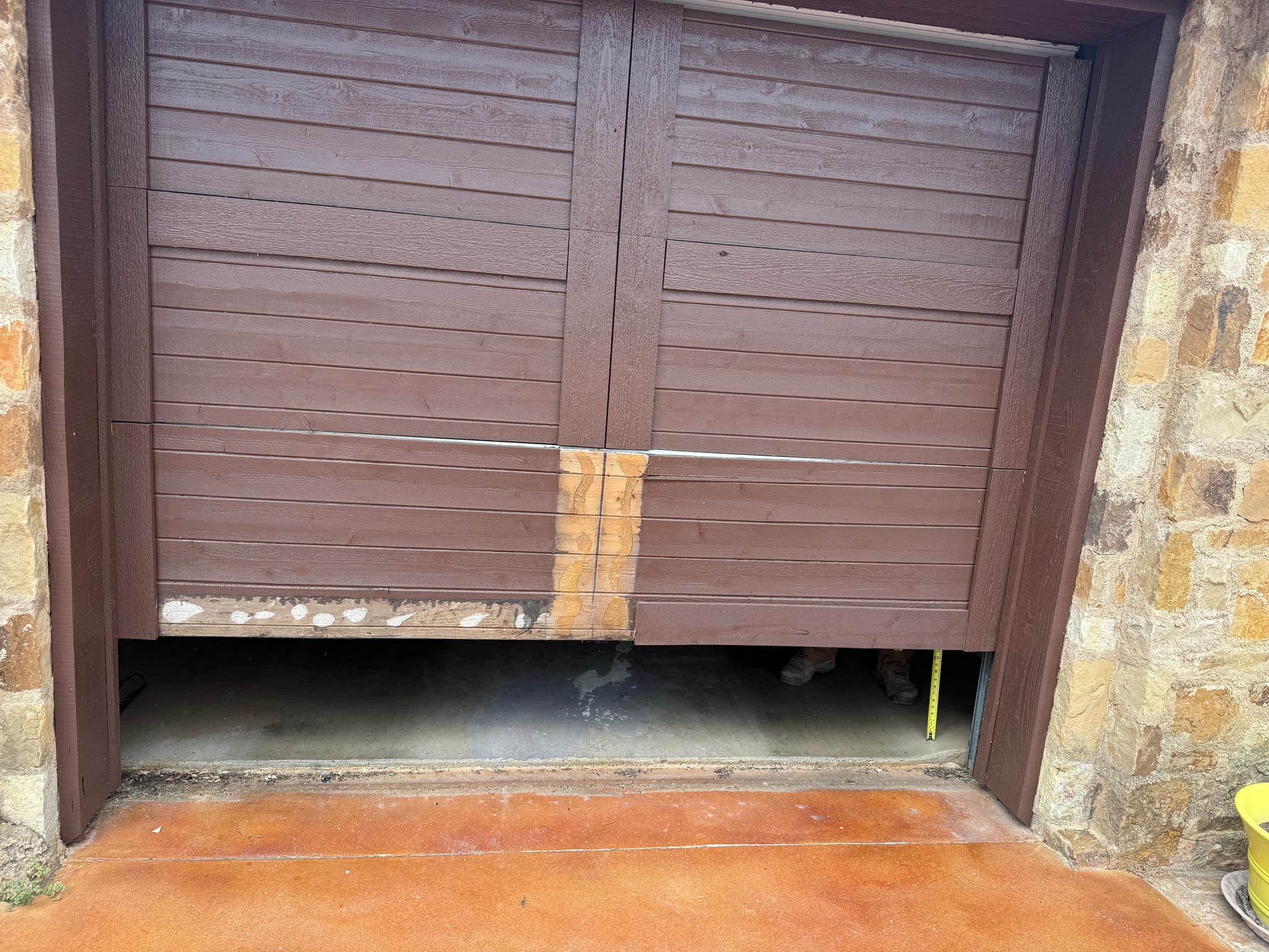 A damaged brown wood carriage house style garage door with a broken bottom panel