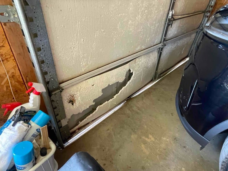 Bottom panel of a white steel garage door with its skin dented and peeling, inside a Marble Falls garage