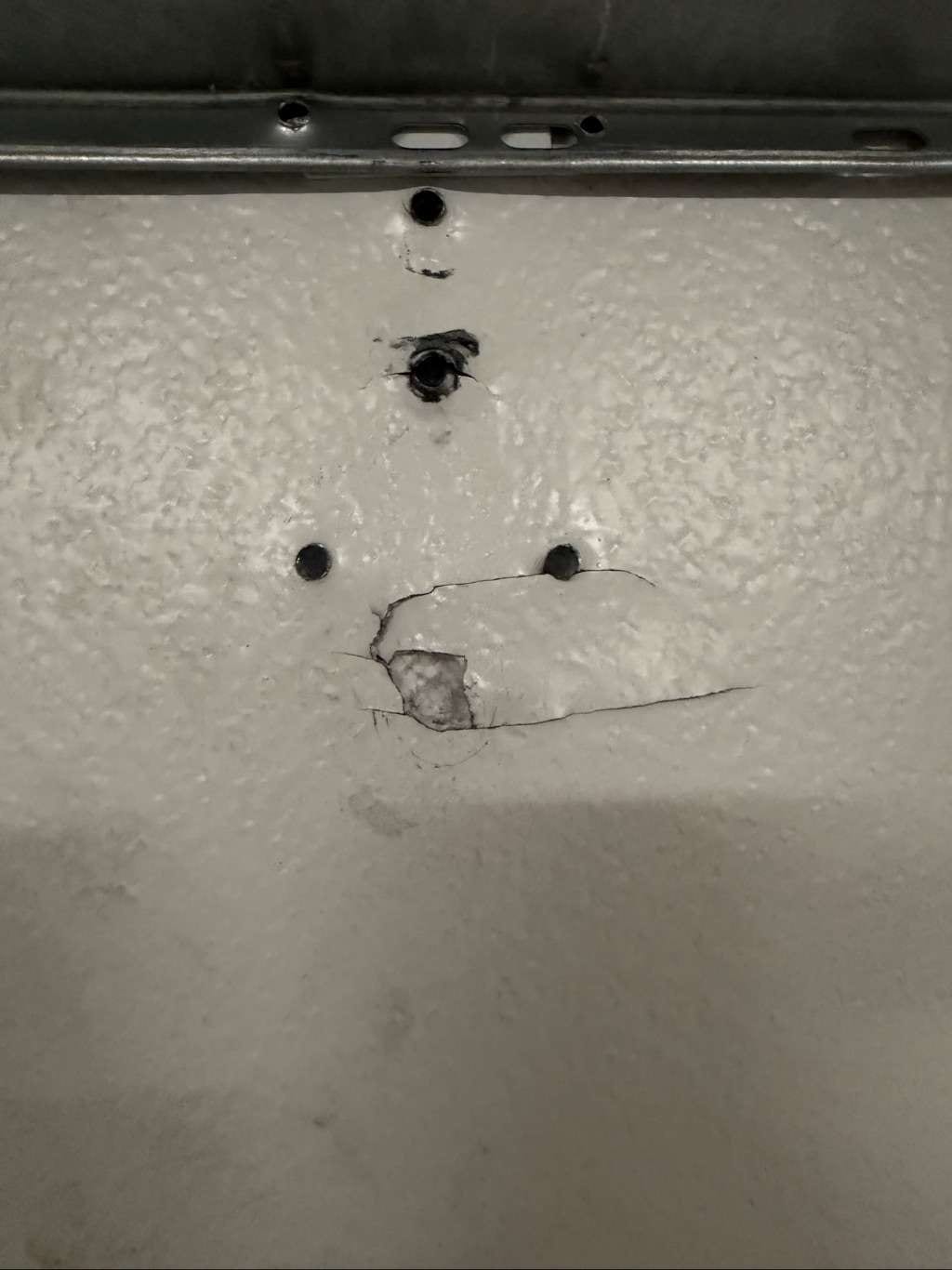 A close up view of a crack and puncture in a white garage door panel, in Horseshoe Bay