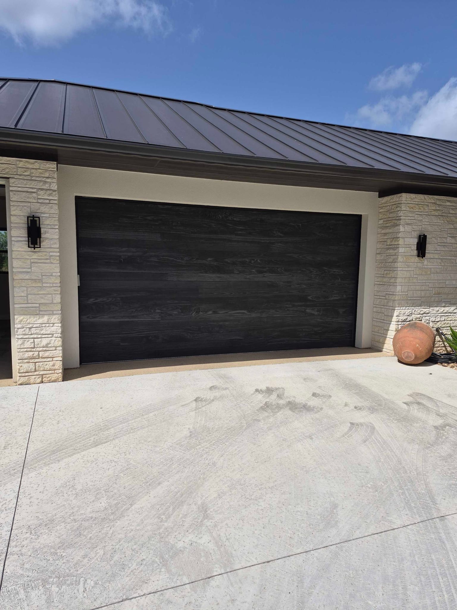 A dark wood grain finish double garage door installed on a modern home with stone accents, in Horseshoe Bay