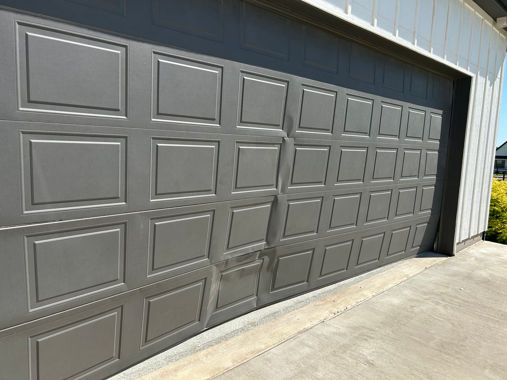 A gray steel raised panel garage door with visible dent damage on the bottom sections