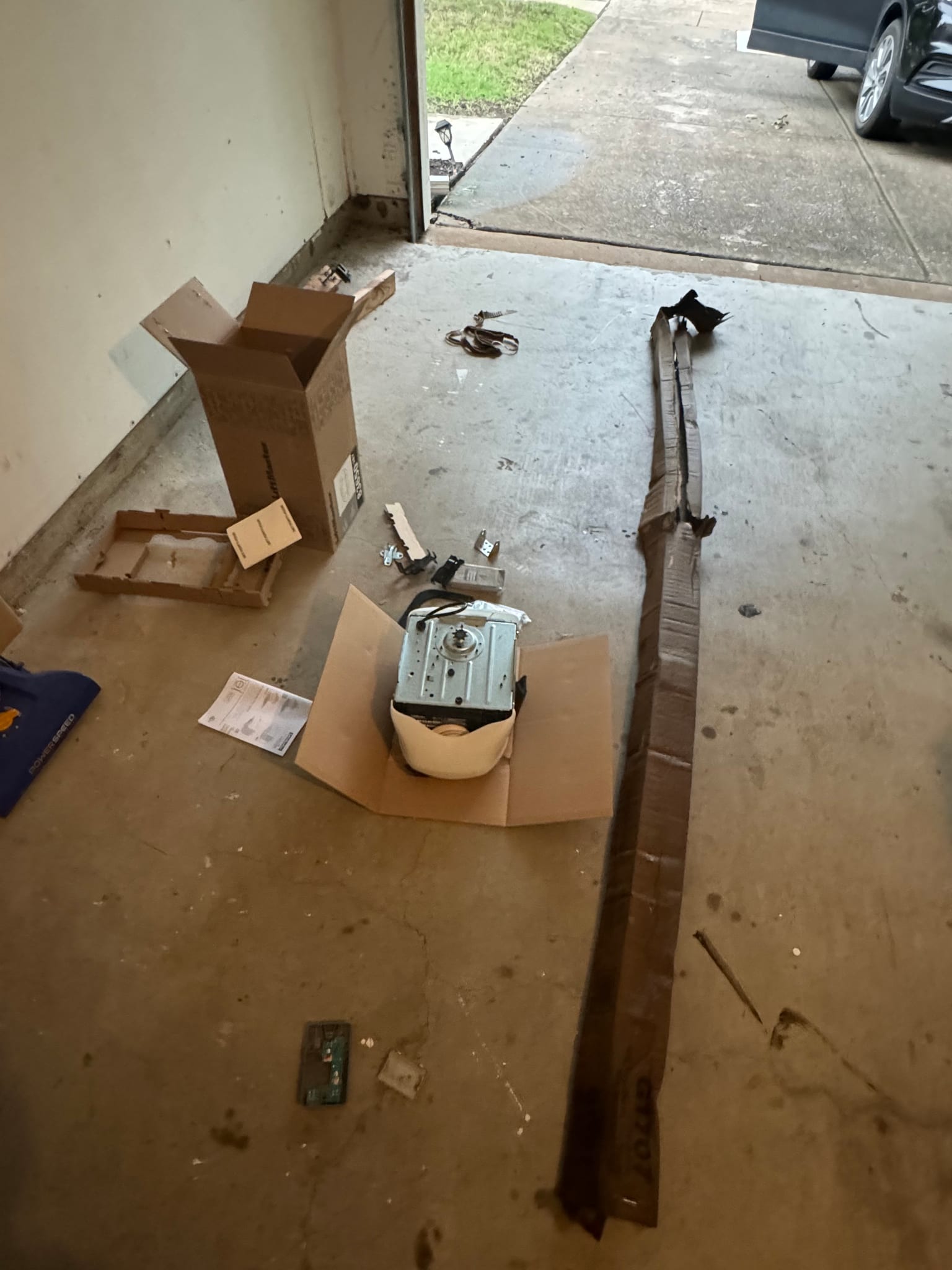 A disassembled garage door opener motor unit and parts on a concrete floor