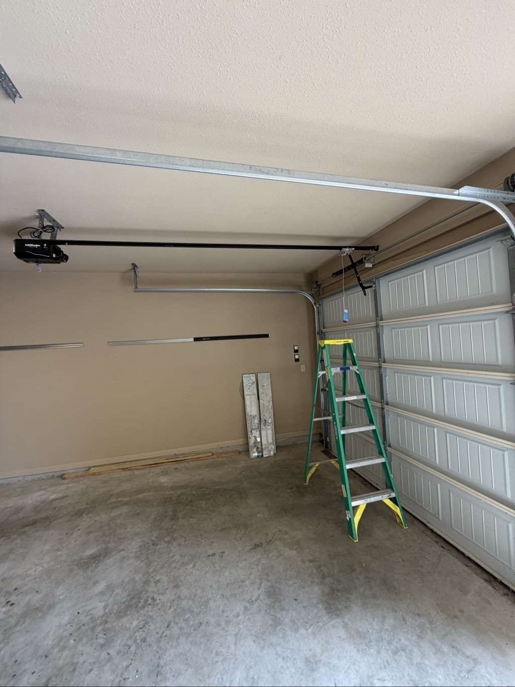 A black garage door opener rail installed along a garage ceiling above a green stepladder, in Horseshoe Bay