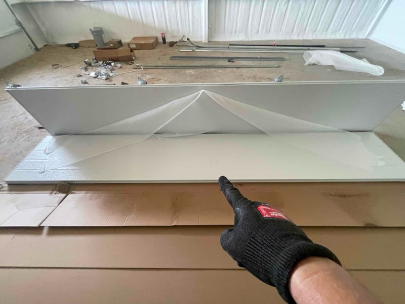 Technician's gloved hand pointing to a new white garage door panel ready for installation in Castell