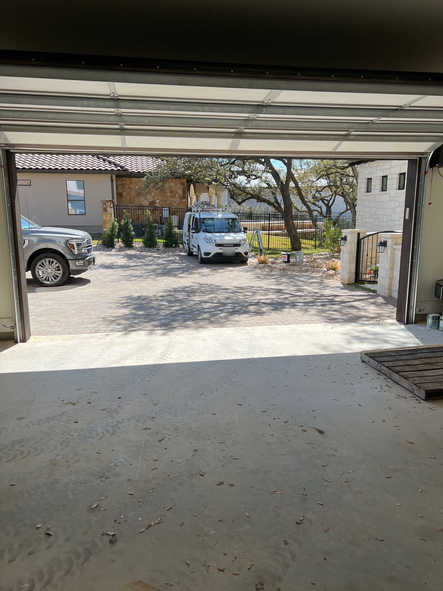An open garage door reveals a paved driveway with a white service van and a silver pickup truck parked outside a stone house, in Marble Falls