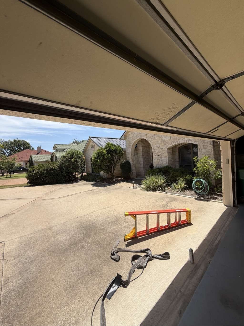 A technician's view from inside a garage looking out at a concrete driveway and a stone residential house, in Horseshoe Bay