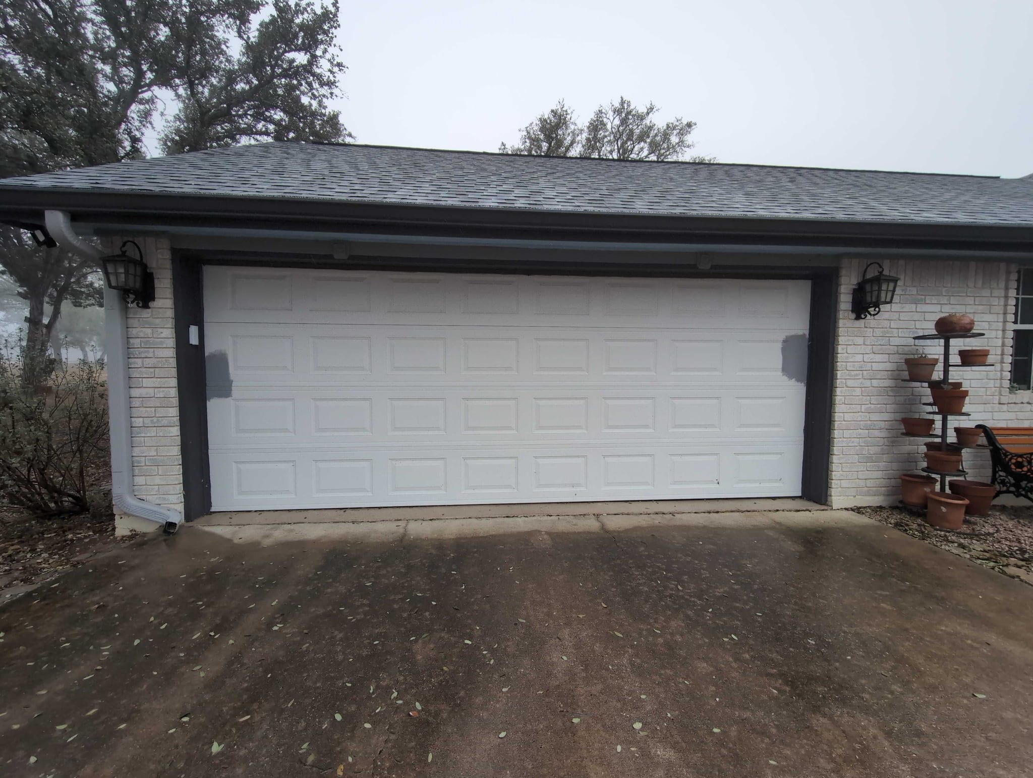 White raised-panel double garage door on a white brick home with a wet concrete driveway in Marble Falls
