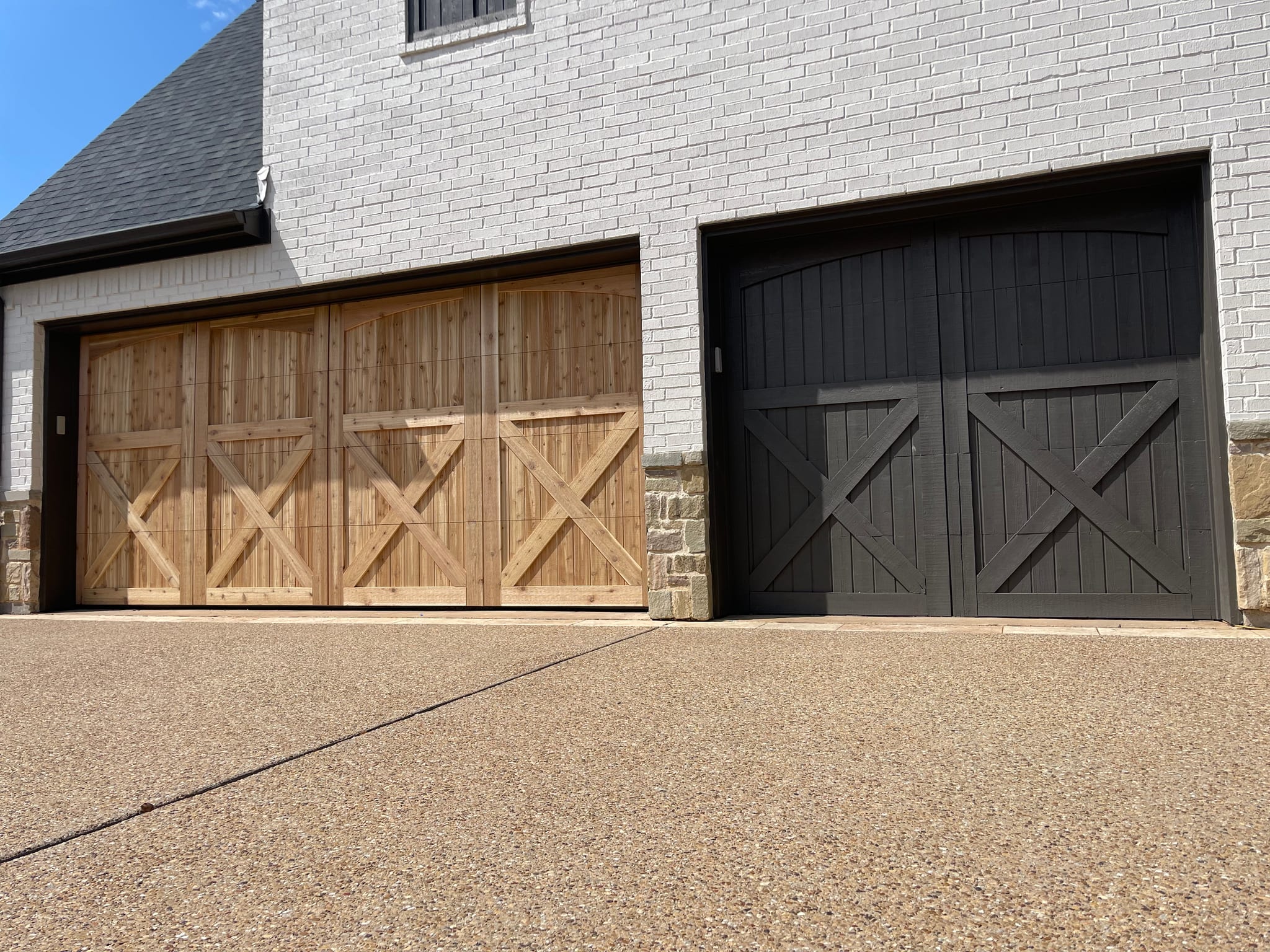 Two separate garage doors featuring carriage house style with X-brace designs, one in natural wood and one in dark charcoal